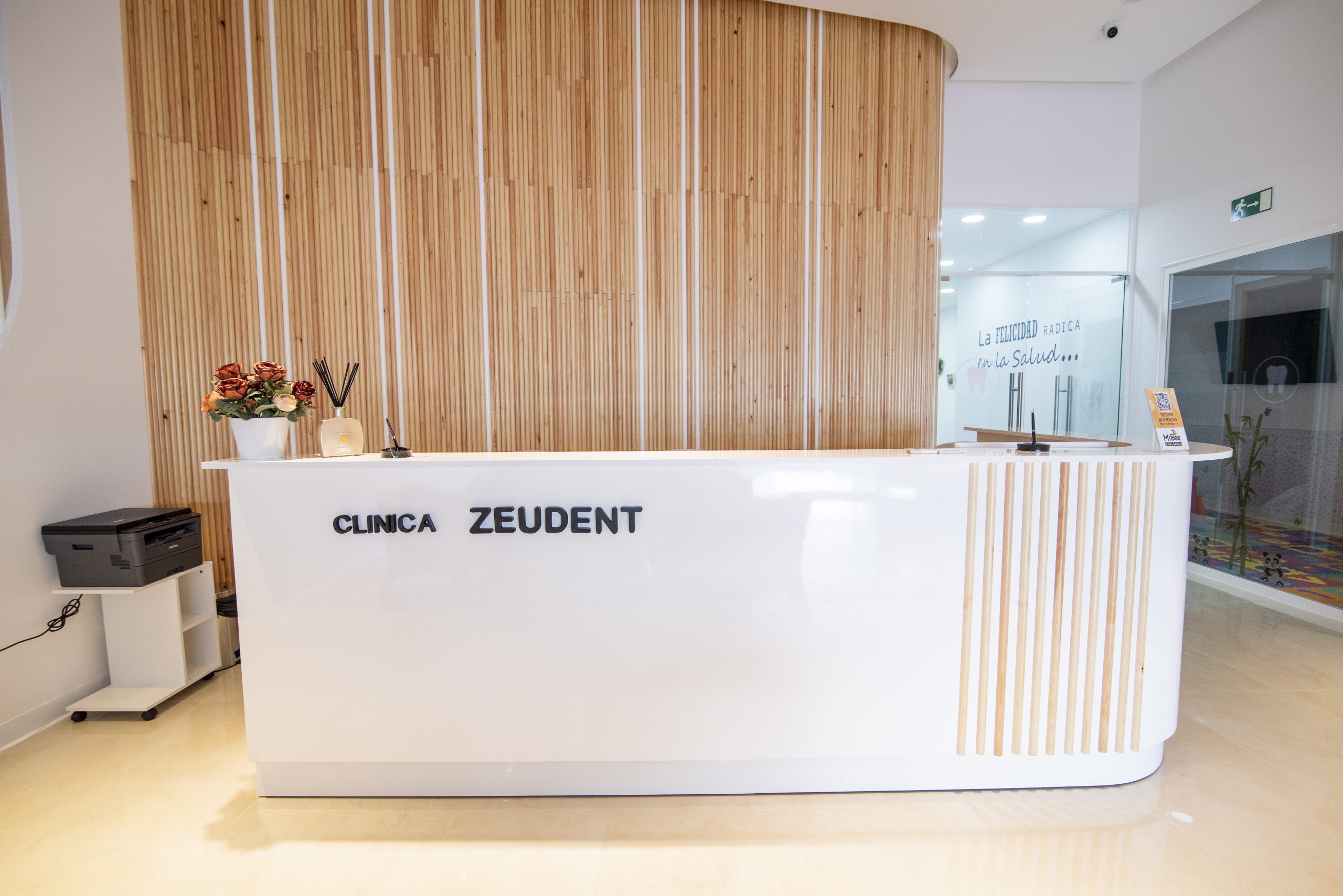 Fotografía de sala de espera de una clínica luminosa, con un gran mostrador blanco y muebles claros