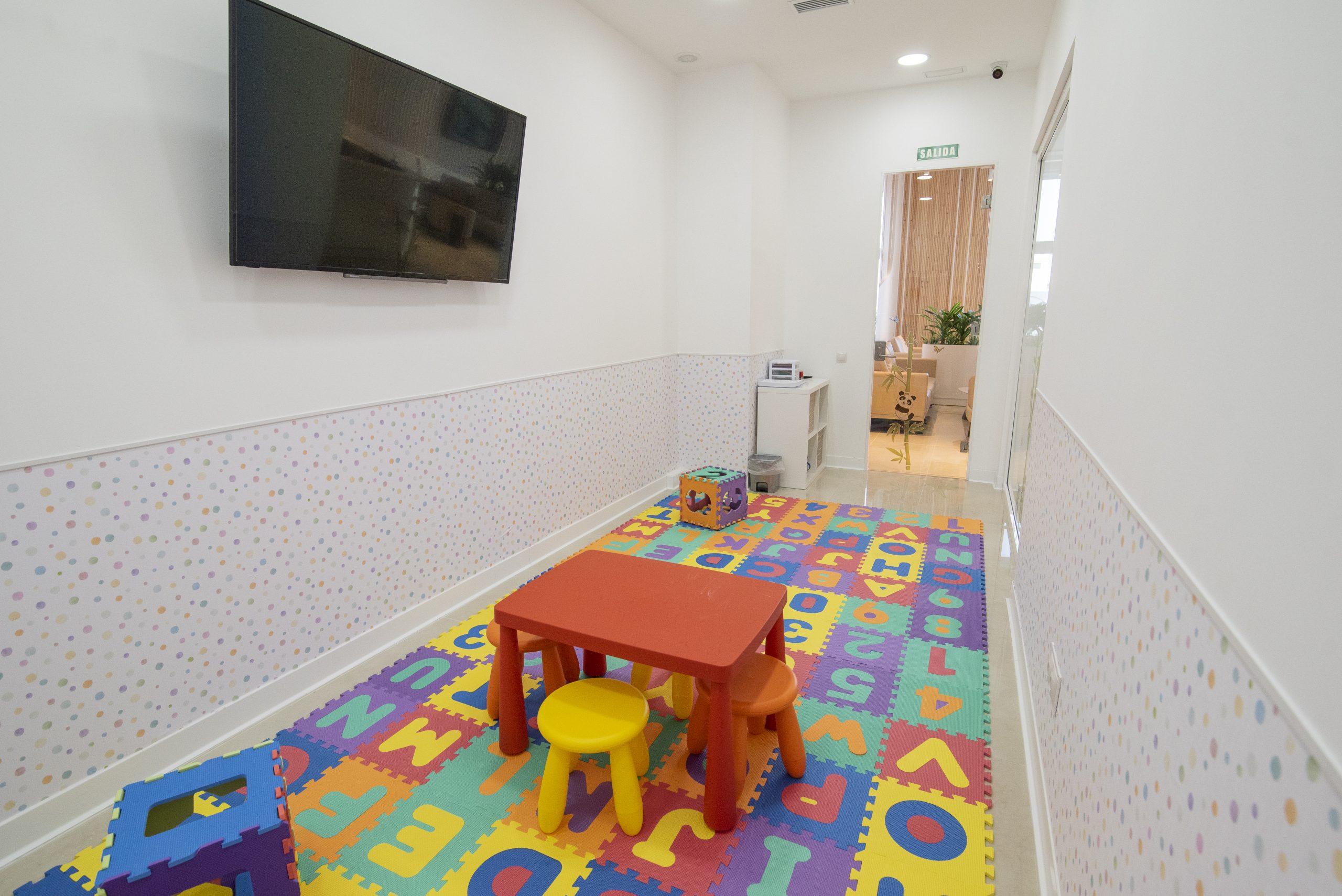 Fotografía de sala de juegos infantil, con mobiliario pequeño y colorido, y paredes blancas